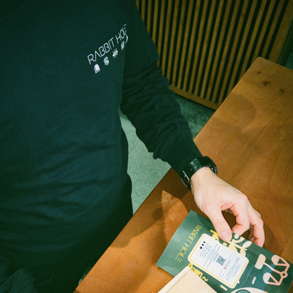 David Lalonde featured wearing a black long sleeve tshirt  with 'Rabbit Hole' text, holding a bag of coffee beans on a wooden table.
